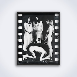 May include: Black and white photograph of a film strip with a scene of three people in a ritual setting. Two women are standing, one with a chalice, and a man is kneeling in front of them.