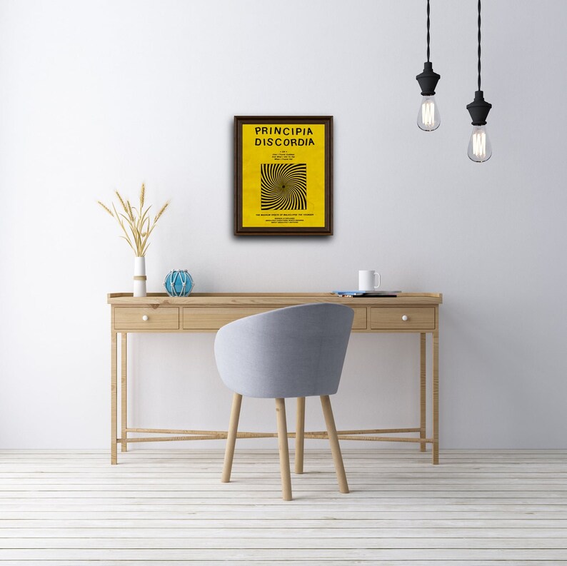 Puede incluir: Una impresi&oacute;n enmarcada de un p&oacute;ster amarillo con texto negro que dice "Principia Discordia" y un dise&ntilde;o en espiral en blanco y negro. El p&oacute;ster est&aacute; colgado en una pared blanca sobre un escritorio de madera con una silla gris.