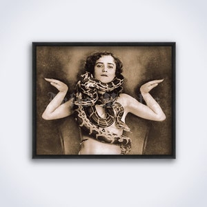 May include: A vintage black and white photograph of a woman with a snake wrapped around her neck and torso. The woman is wearing a simple garment and has her arms outstretched.