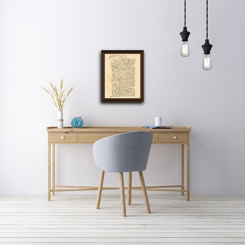 May include: A framed document with handwritten text in blue ink. The document is titled "Declaration of Independence" and is displayed on a white wall above a wooden desk with a chair.