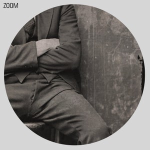May include: A black and white photo of a person sitting with their arms crossed, wearing a suit and pants. The person is sitting against a wall with a textured surface.
