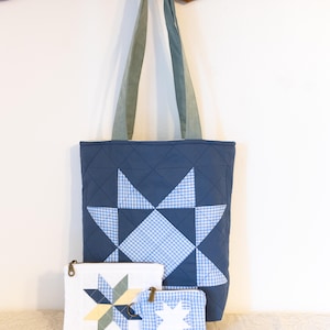 May include: A quilted tote bag in slate blue with a large central star pattern in light blue gingham and solid blue fabric, accompanied by a medium white zippered pouch and a small blue gingham zippered pouch, both featuring star designs.