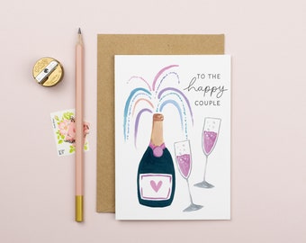 May include: A white card with a hand-painted illustration of a champagne bottle with a pink heart on the label. The bottle is popping open with a rainbow of colors. Two champagne flutes are next to the bottle. The card says "To the happy couple" in black script.