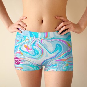 May include: Abstract swirl-patterned shorts in shades of blue, white, and pink. The shorts feature a dynamic design with a pink splash and a snowboarder graphic. Made from a stretchy fabric.
