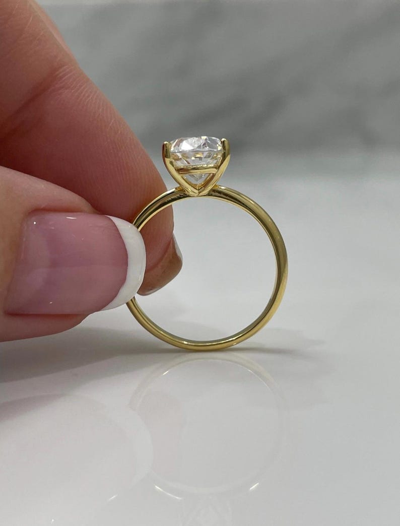 Puede incluir: Un anillo de compromiso solitario de oro con un diamante redondo brillante.