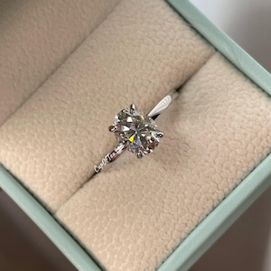 May include: A silver ring with a large oval-shaped diamond in a ring box. The ring is in a light blue box with a white interior.