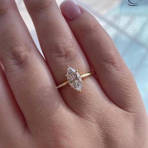 K&ouml;nnte beinhalten: Ein goldener Ring mit einem gro&szlig;en, klaren, markisenf&ouml;rmigen Diamanten.
