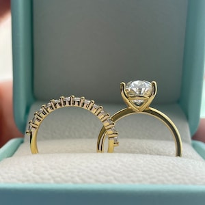 May include: A pair of gold wedding bands with sparkling diamonds. The engagement ring features a large, round center stone and smaller diamonds set in a pave band. The wedding band is a simple band with a row of diamonds.