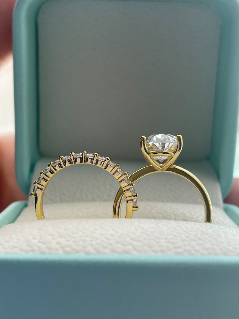 May include: A pair of gold wedding bands with sparkling diamonds. The engagement ring features a large, round center stone and smaller diamonds set in a pave band. The wedding band is a simple band with a row of diamonds.