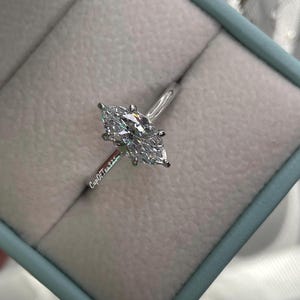 K&ouml;nnte beinhalten: Ein silberner Ring mit einem Marquise-Diamanten in einer hellblauen Ringbox. Die Ringbox hat den Text "CupOfTears" an der Seite.