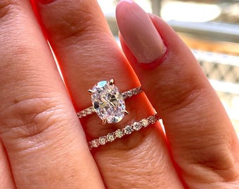 May include: A rose gold engagement ring set featuring a large oval-cut center stone held by four prongs on a delicate pavé band, paired with a matching eternity band encrusted with small round-cut stones that sparkle in the light.
