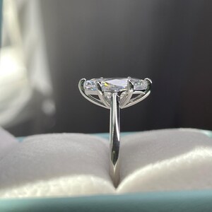 K&ouml;nnte beinhalten: Ein silberner Ring mit einem gro&szlig;en ovalen Diamanten, der in einer dreifach-Krappenfassung sitzt. Der Ring befindet sich in einer hellblauen Ringbox.