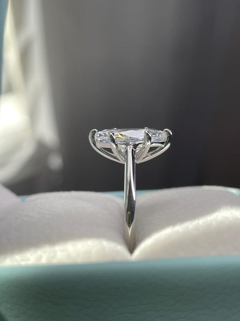 K&ouml;nnte beinhalten: Ein silberner Ring mit einem gro&szlig;en ovalen Diamanten, der in einer dreifach-Krappenfassung sitzt. Der Ring befindet sich in einer hellblauen Ringbox.