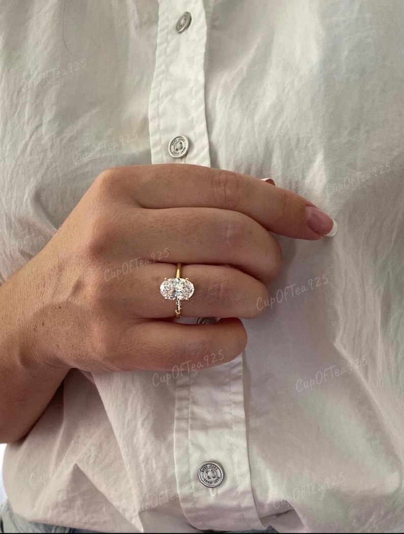 Puede incluir: Un anillo de oro con una gran piedra preciosa ovalada transparente rodeada de piedras preciosas transparentes m&aacute;s peque&ntilde;as.