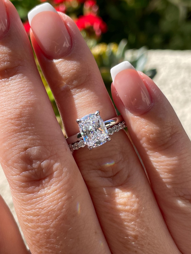 May include: A silver-toned ring set featuring a large, rectangular cushion-cut center stone held by four prongs on a smooth band, paired with a matching eternity band adorned with a row of small, round, brilliant-cut stones.