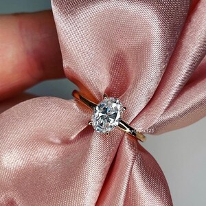 Puede incluir: Un anillo de oro con una gran piedra preciosa ovalada transparente. El anillo est&aacute; sobre una tela de sat&eacute;n rosa.