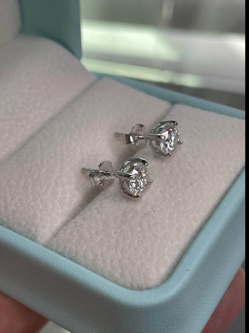 May include: A pair of silver stud earrings with clear round stones. The earrings are in a light blue box with white lining.