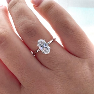 Puede incluir: Un anillo de plata con un diamante de forma ovalada engastado en garras. El anillo est&aacute; en el dedo de una persona.