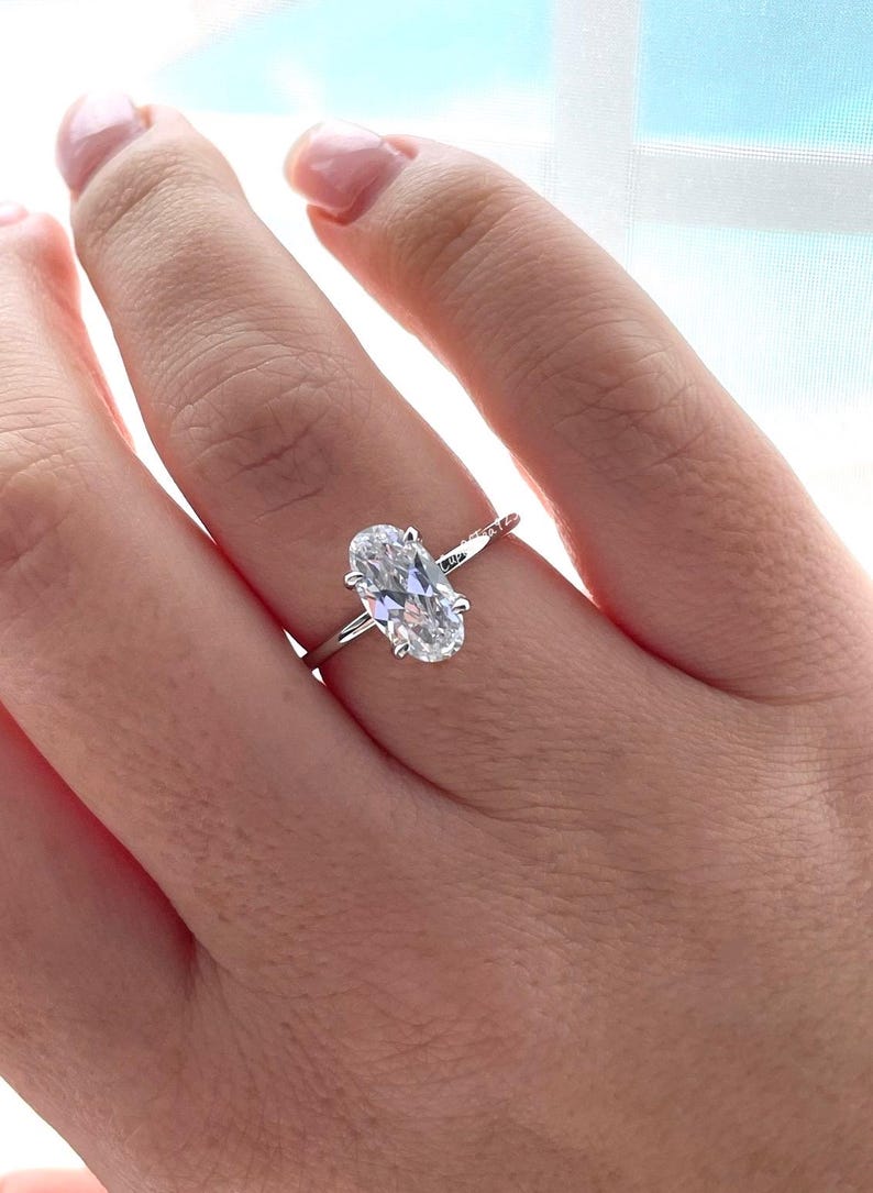 Puede incluir: Un anillo de plata con un diamante de forma ovalada engastado en garras. El anillo est&aacute; en el dedo de una persona.