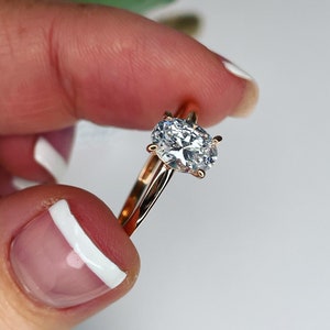 Puede incluir: Un anillo de compromiso de oro rosa con un gran diamante de forma ovalada.