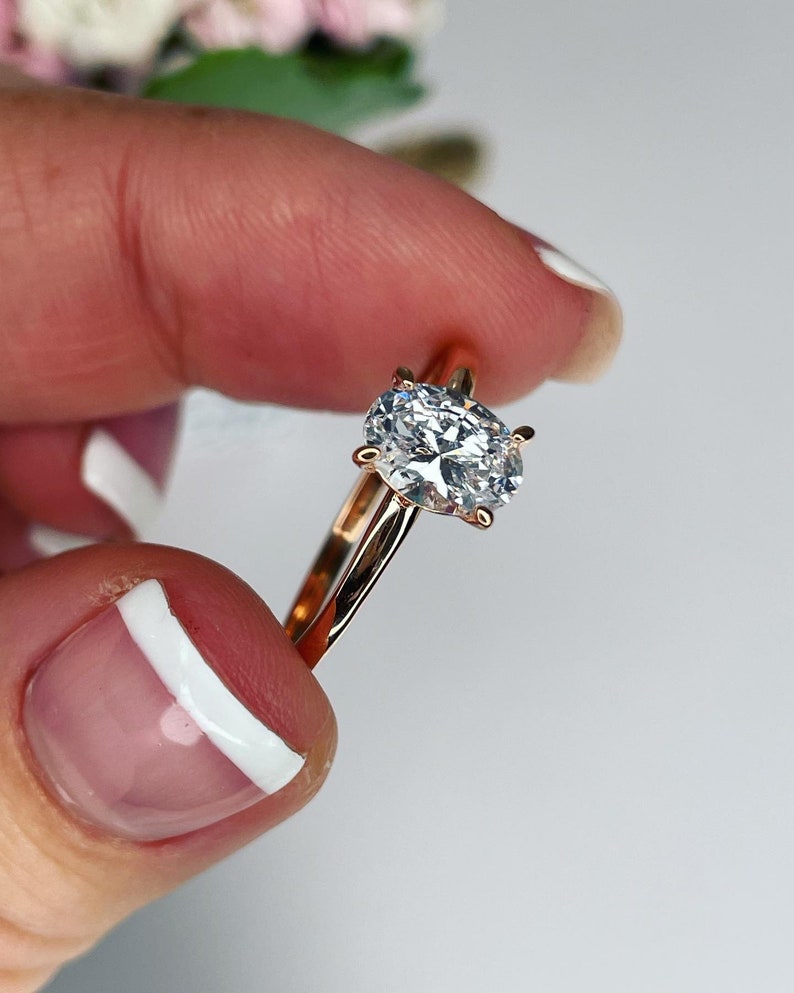 Puede incluir: Un anillo de compromiso de oro rosa con un gran diamante de forma ovalada.