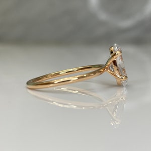 Puede incluir: Un anillo de compromiso de oro con un gran diamante ovalado transparente. El anillo est&aacute; engastado en una banda fina.