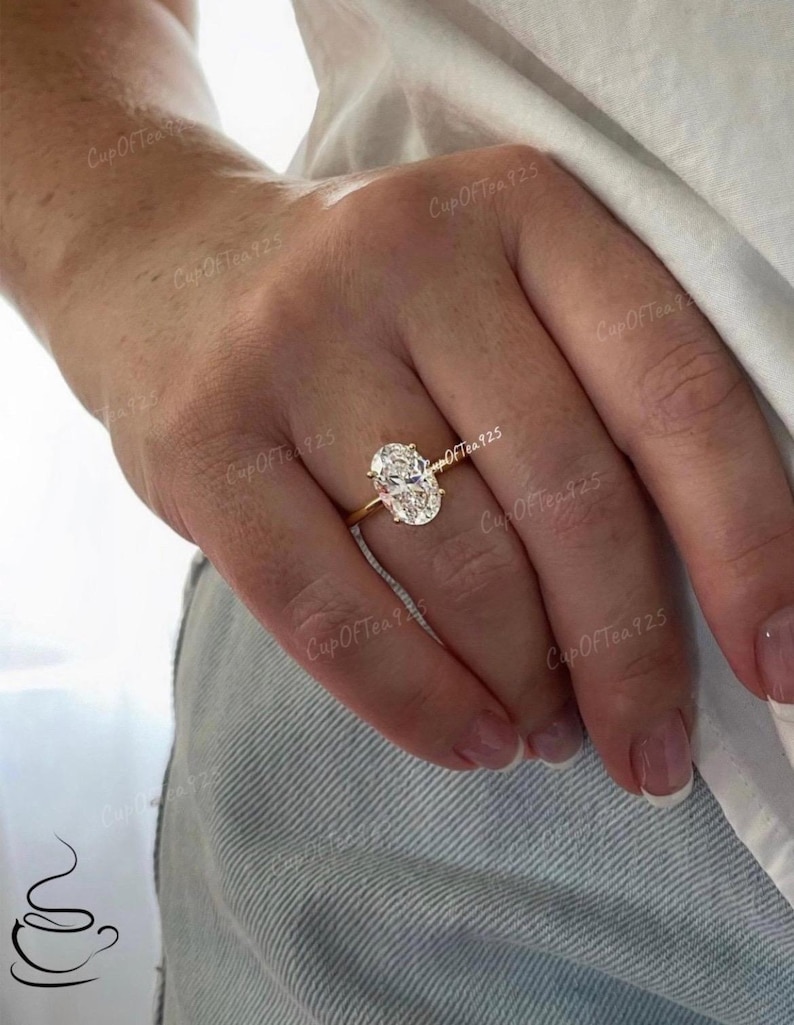 Puede incluir: Un anillo de oro con una gran piedra preciosa ovalada transparente. El anillo est&aacute; en el dedo de una persona.