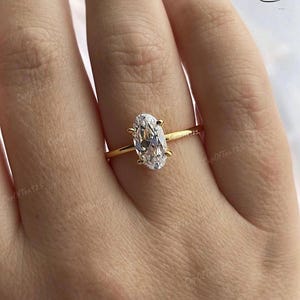 Puede incluir: Un anillo de oro con una gran piedra preciosa ovalada transparente. El anillo est&aacute; en el dedo de una persona.