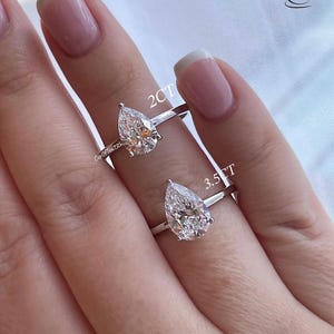 K&ouml;nnte beinhalten: Zwei birnenf&ouml;rmige Diamant-Verlobungsringe an einer Hand. Der Ring links hat einen 2 Karat Diamanten und der Ring rechts einen 3,5 Karat Diamanten.