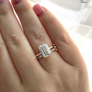 May include: A gold ring featuring a large, clear emerald-cut diamond and a smaller diamond band.