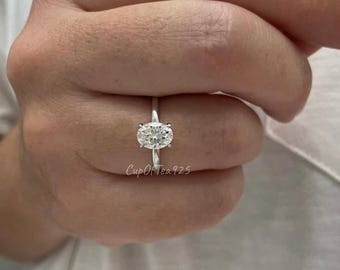 May include: A silver ring with a large oval-shaped clear gemstone. The ring is on a person's finger.