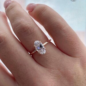 Puede incluir: Un anillo de oro rosa con una gran piedra preciosa ovalada transparente. El anillo est&aacute; en el dedo de una persona.