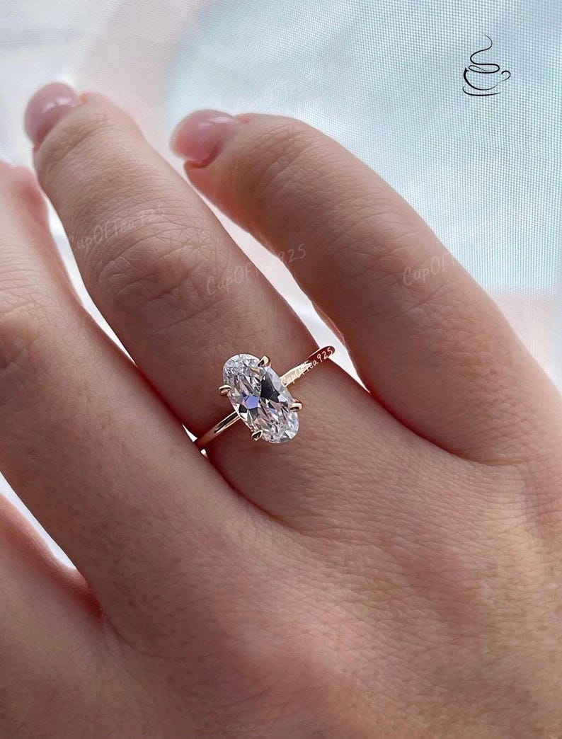Puede incluir: Un anillo de oro rosa con una gran piedra preciosa ovalada transparente. El anillo est&aacute; en el dedo de una persona.