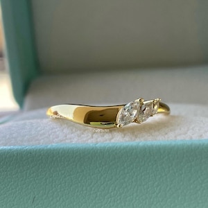 May include: A gold ring with three marquise-cut gemstones. The ring has a smooth, polished band and the gemstones are set in a cluster. The ring is displayed in a light blue box.