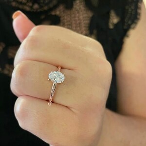 Puede incluir: Un anillo de compromiso de oro rosa con un diamante de forma ovalada.