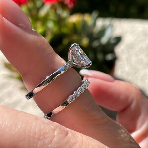 May include: A silver-toned engagement ring featuring a large, elongated rectangular center stone set in a high-profile basket, paired with a matching silver-toned wedding band adorned with a row of seven small, round, brilliant-cut clear stones.