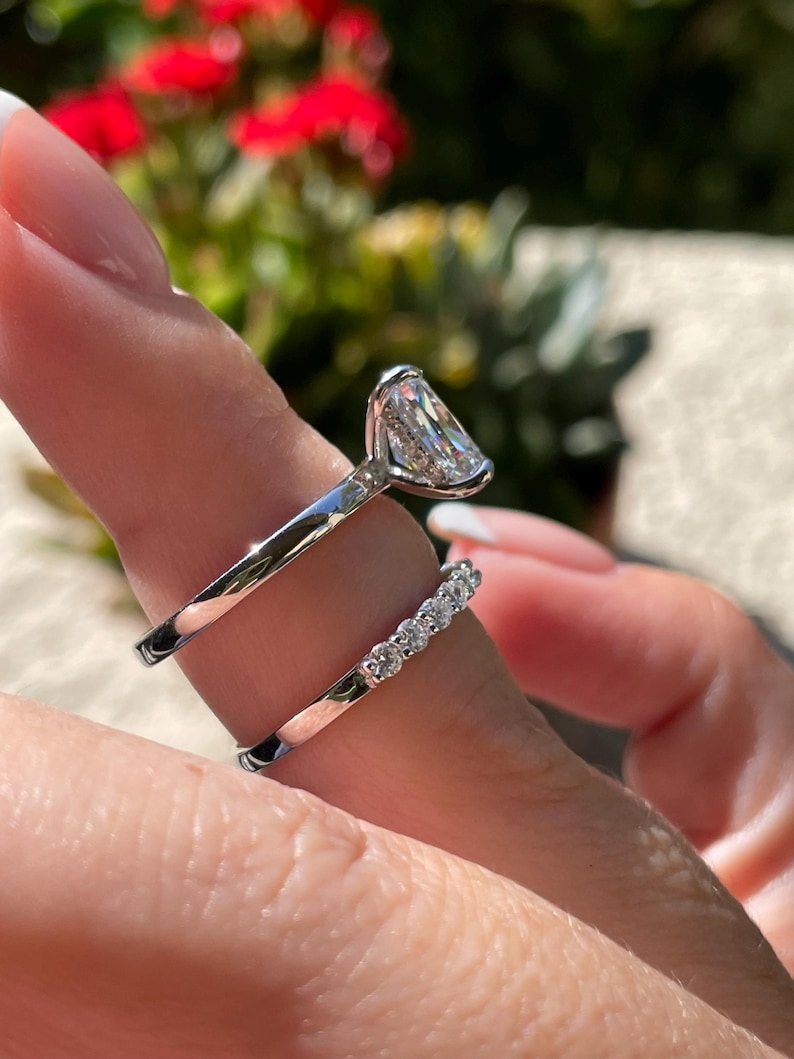May include: A silver-toned engagement ring featuring a large, elongated rectangular center stone set in a high-profile basket, paired with a matching silver-toned wedding band adorned with a row of seven small, round, brilliant-cut clear stones.