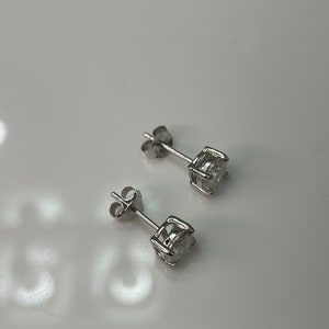 May include: A pair of silver stud earrings with a clear round stone in the center of each earring.