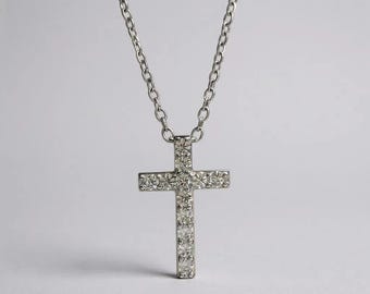 May include: A silver-toned cross pendant necklace. The cross is encrusted with small, sparkling stones. The chain is a simple link style, and the background is a plain white.