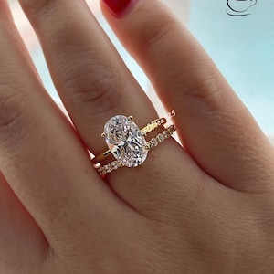 May include: A gold ring with a large oval-shaped clear gemstone. The ring is set with smaller clear gemstones around the band. The ring is worn on a person's finger.