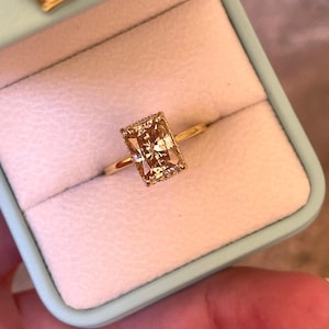 May include: A gold ring featuring a large, rectangular, champagne-colored gemstone with a faceted surface, set in a delicate gold band. The ring is presented inside a light blue, velvet-lined jewelry box with a gold crown emblem on the lid.