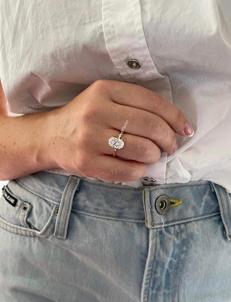 Puede incluir: Un anillo de oro con un gran diamante de forma ovalada. El anillo est&aacute; en el dedo de una persona.