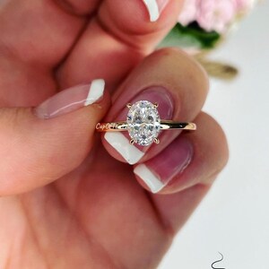 Puede incluir: Un anillo de oro con una gran piedra preciosa ovalada transparente. El anillo est&aacute; en un dedo con esmalte de u&ntilde;as blanco.