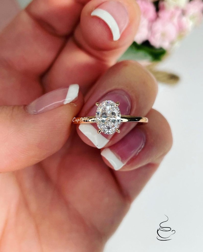 Puede incluir: Un anillo de oro con una gran piedra preciosa ovalada transparente. El anillo est&aacute; en un dedo con esmalte de u&ntilde;as blanco.