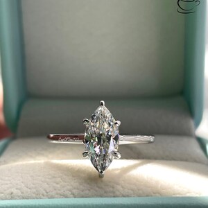 K&ouml;nnte beinhalten: Ein silberner Ring mit einem Marquise-f&ouml;rmigen Diamanten in einer Ringbox. Der Ring befindet sich in einer hellblauen Box mit dem Text "CupOfTea925" im Inneren.