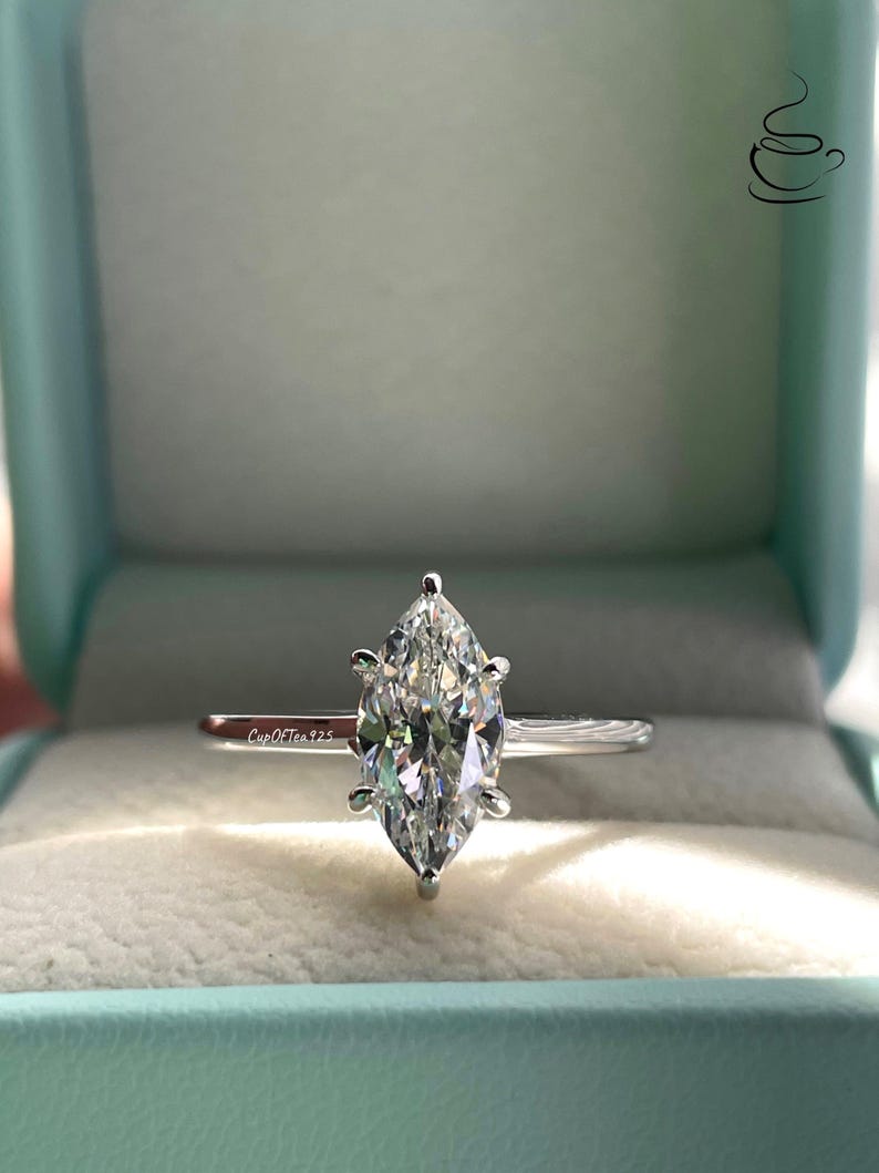 K&ouml;nnte beinhalten: Ein silberner Ring mit einem Marquise-f&ouml;rmigen Diamanten in einer Ringbox. Der Ring befindet sich in einer hellblauen Box mit dem Text "CupOfTea925" im Inneren.
