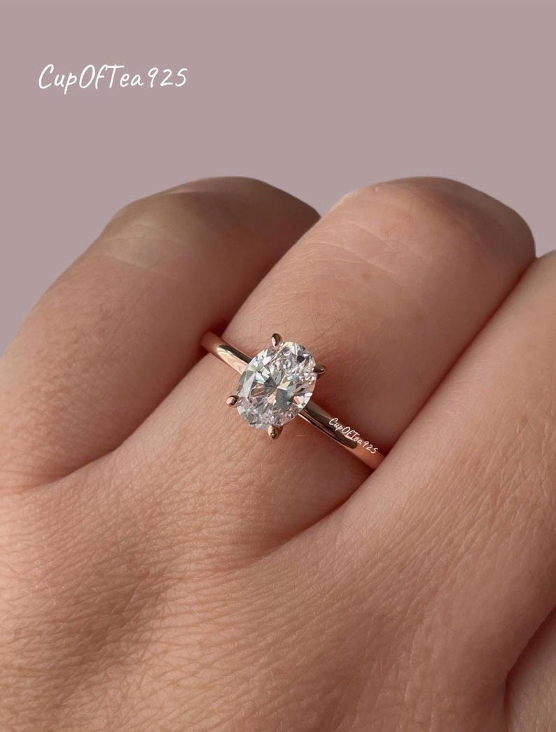Puede incluir: Un anillo de oro rosa con una piedra preciosa ovalada transparente. El anillo est&aacute; grabado con el texto "CupOfTea925".