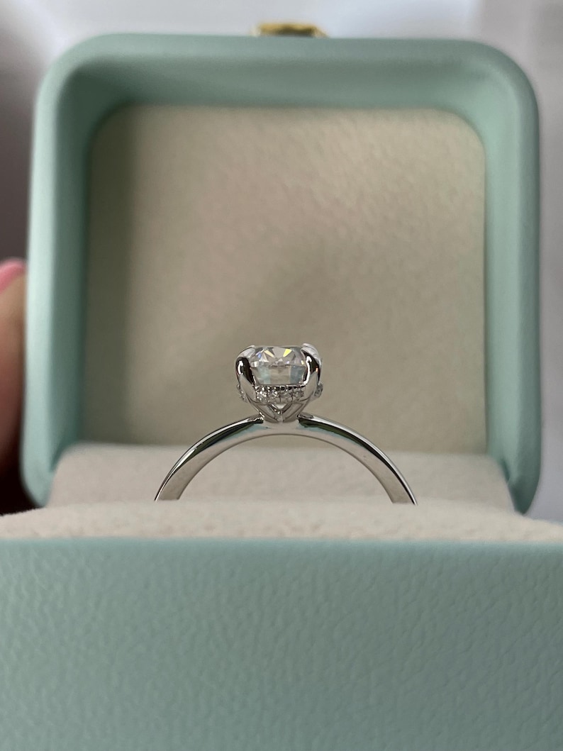 May include: A silver engagement ring with a round, clear diamond in a prong setting. The ring is in a light blue ring box.