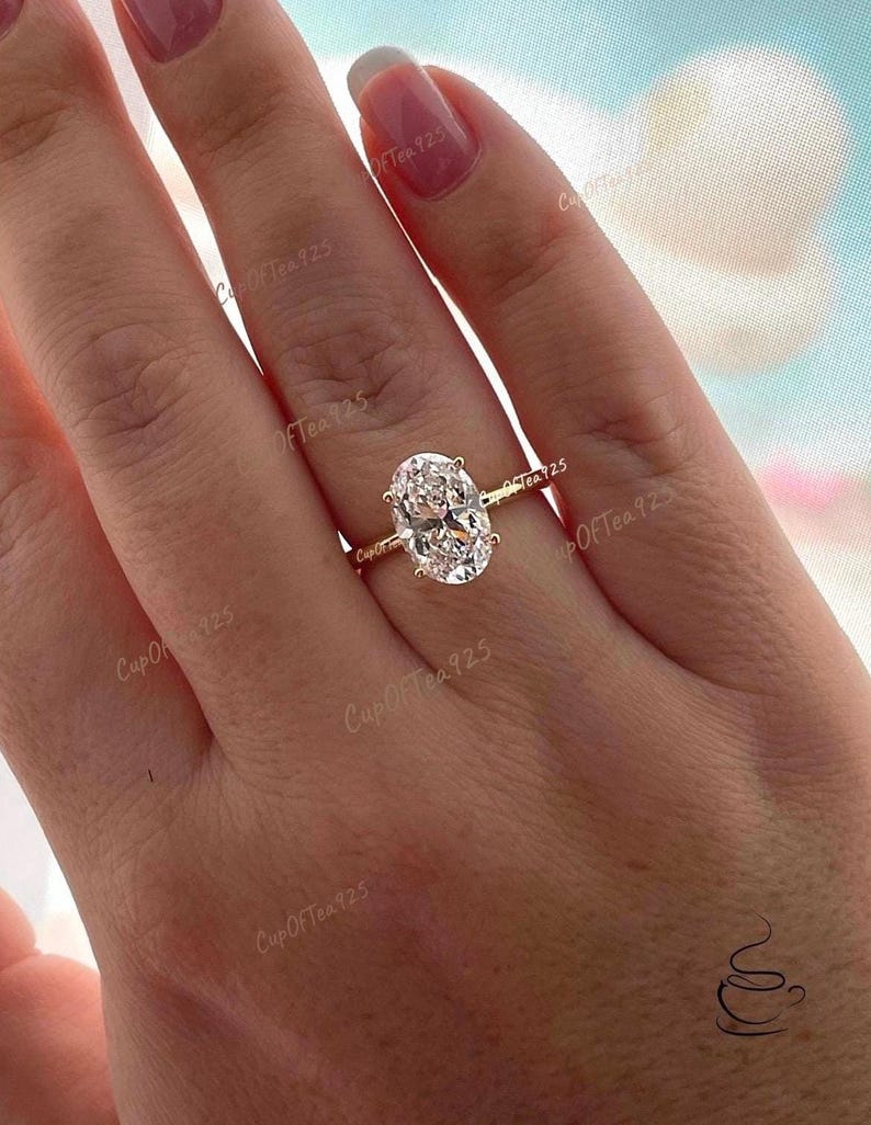Puede incluir: Un anillo de oro con una gran piedra preciosa ovalada transparente. El anillo est&aacute; en el dedo de una persona.
