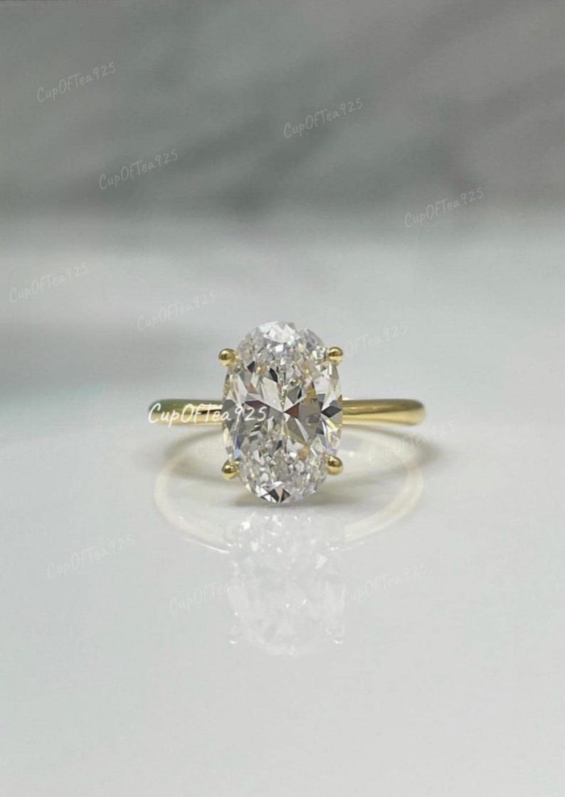 Puede incluir: Un anillo de oro con un diamante de forma ovalada. El diamante es transparente y tiene un corte brillante.